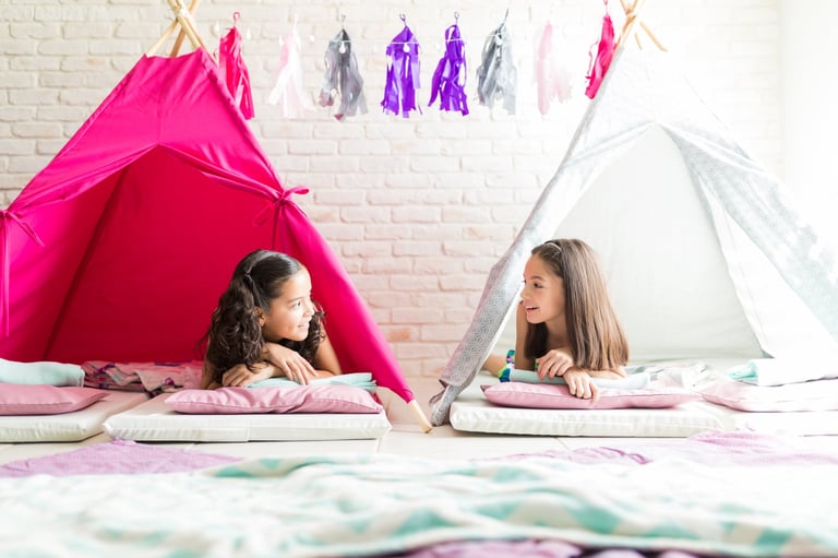 Girls in white teepee tents at a cozy indoor slumber party with soft bedding