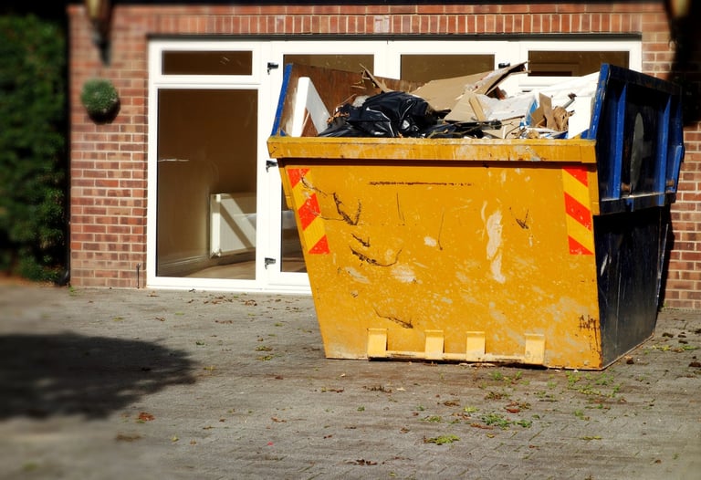 Industrial yellow rubbish skip near house with construction materials