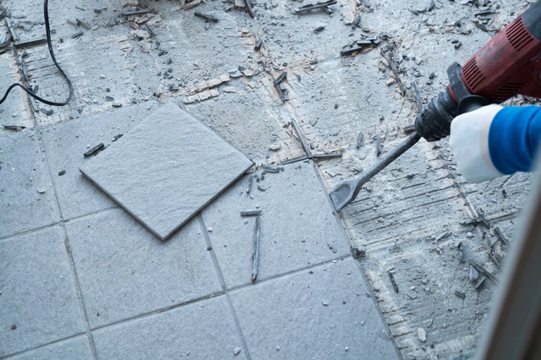 Construction worker using a handheld demolition hammer to chip away and remove old floor tiles