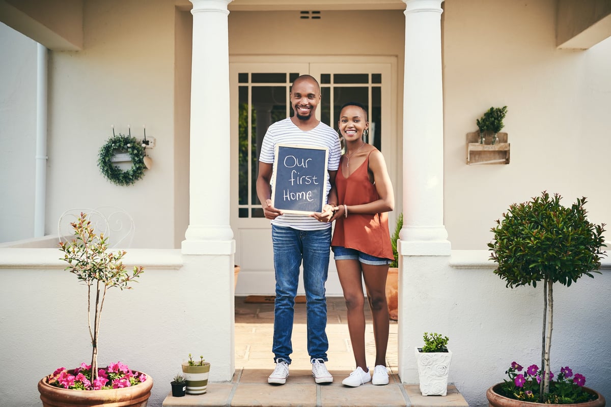 Young couple holding a chalkboard reading our first home, celebrating homeownership