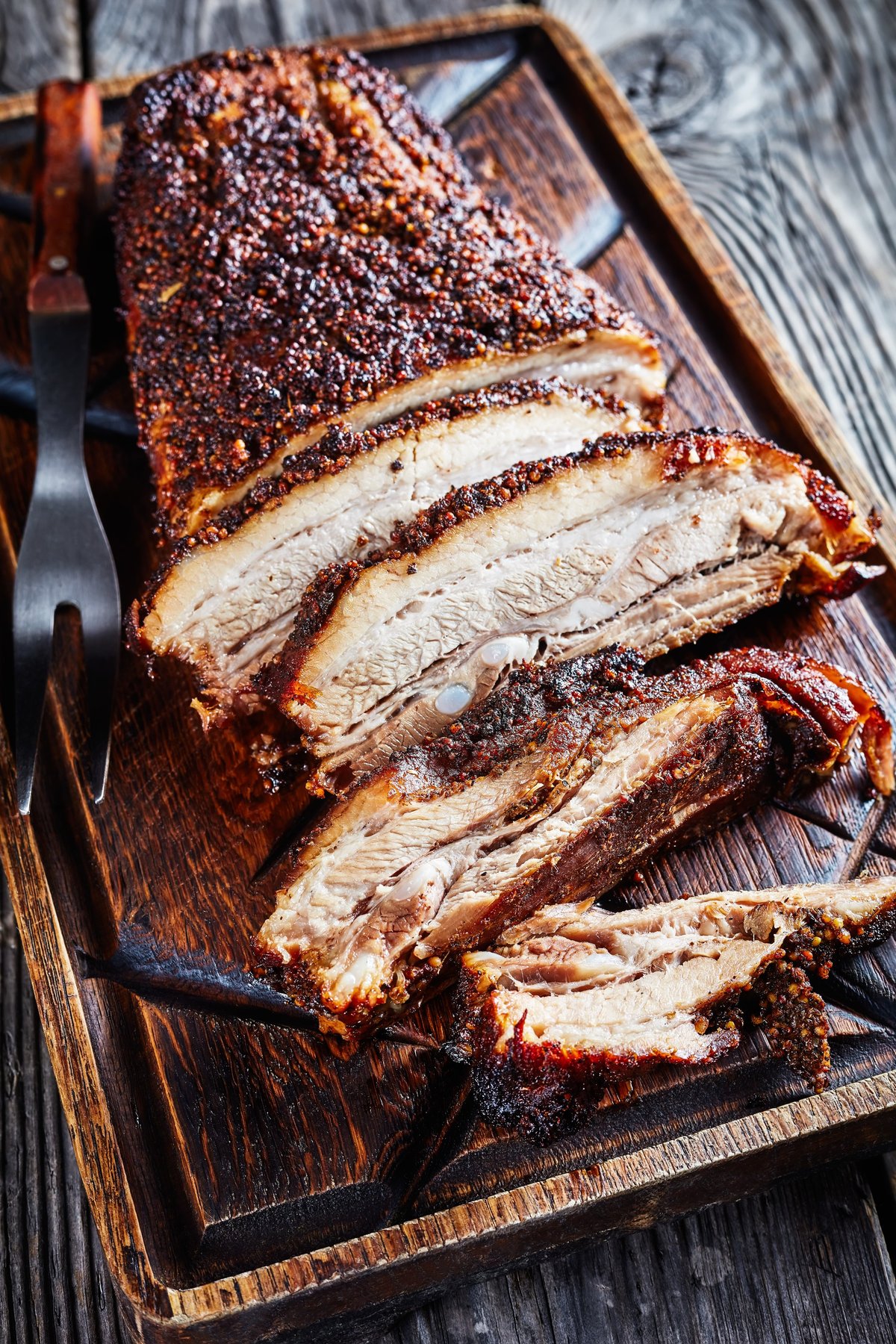 Sliced smoked brisket with dark bark served on a rustic wooden board