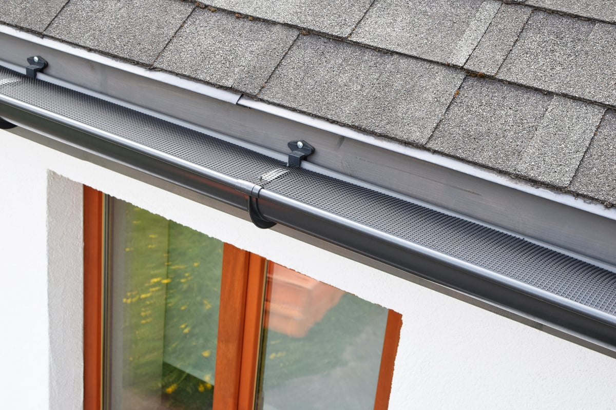 Plastic guard over new dark grey rain gutter on asphalt shingles roof