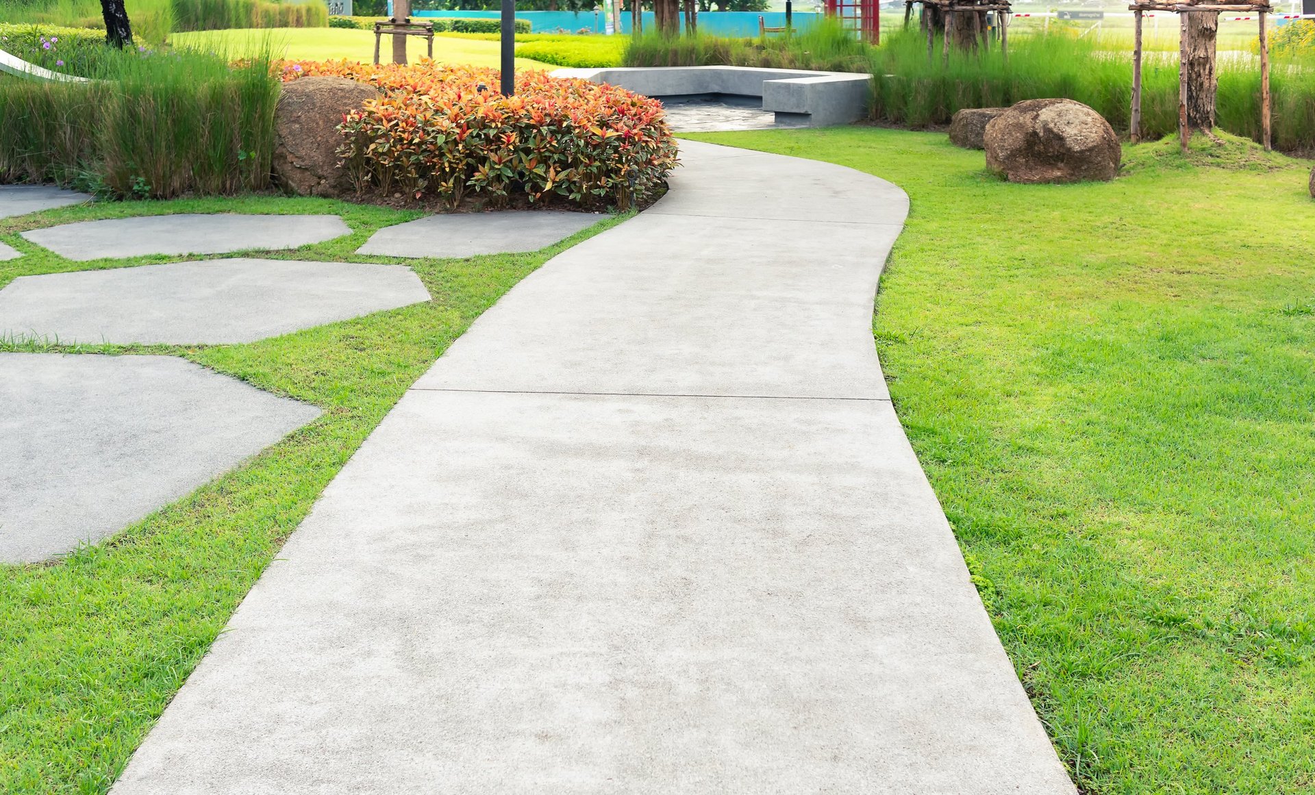 Curved walkway winding through a lush garden with bushes, lawn, and natural landscaping.
