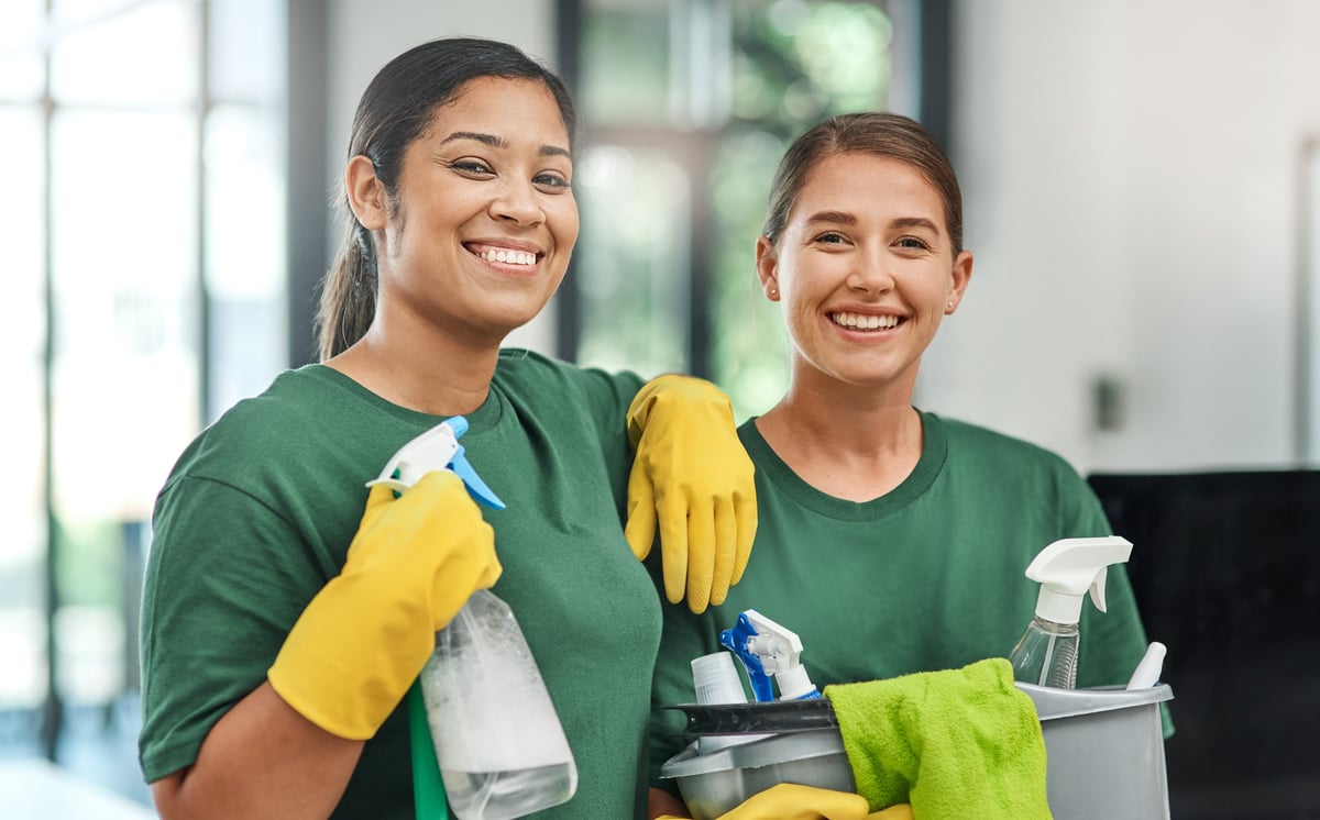 Two professional female cleaners in a modern office, one of Central American descent, smiling confidently