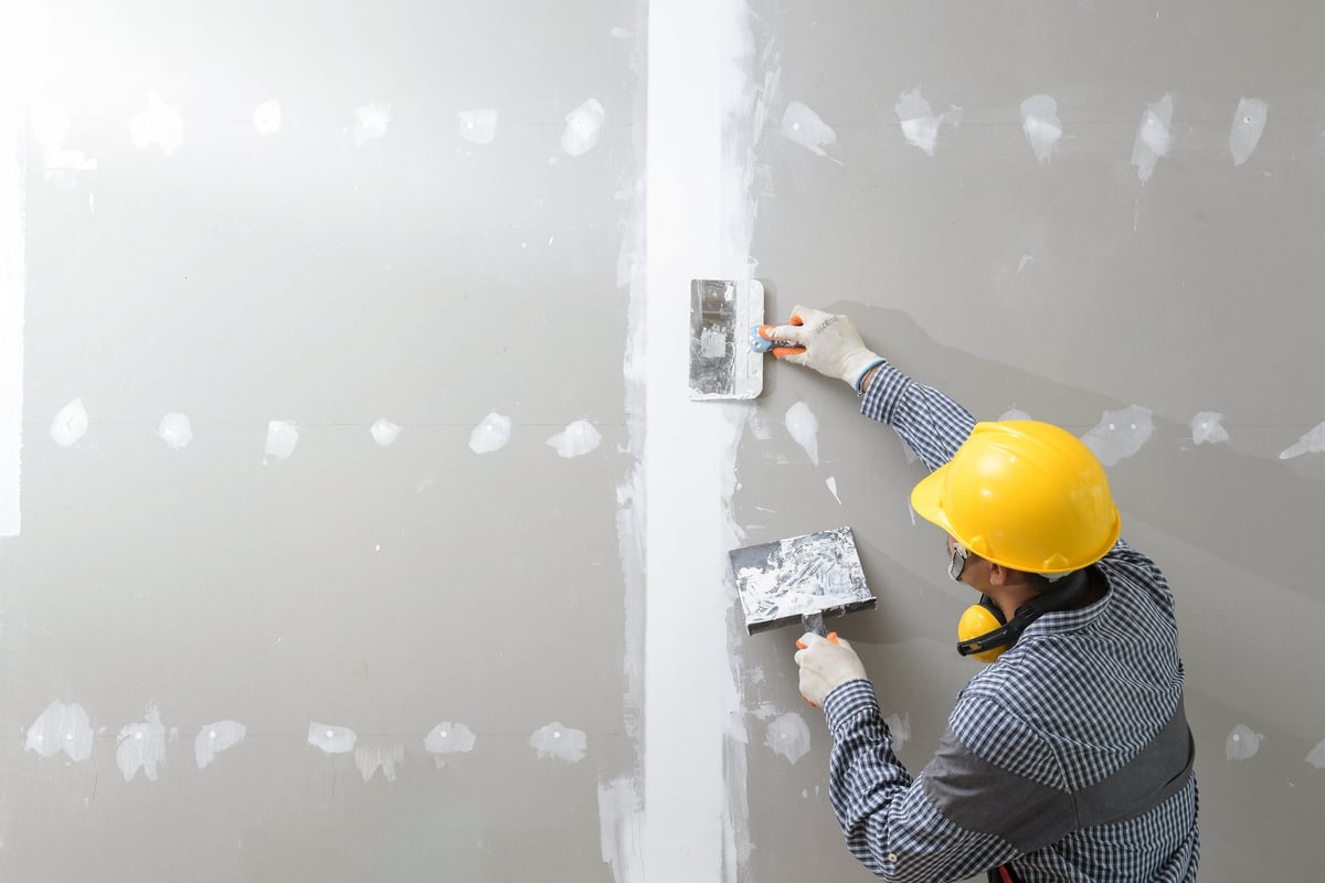 Miro Build construction company flyer showcasing drywall finishing, machine and hand plastering, sanding, and painting services with worker photos and contact number.
