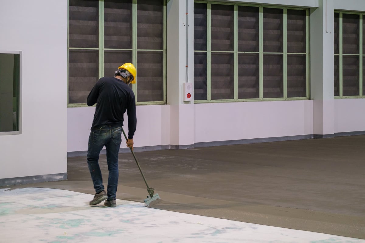 Construction worker using trowel to spread epoxy primer during floor coating installation