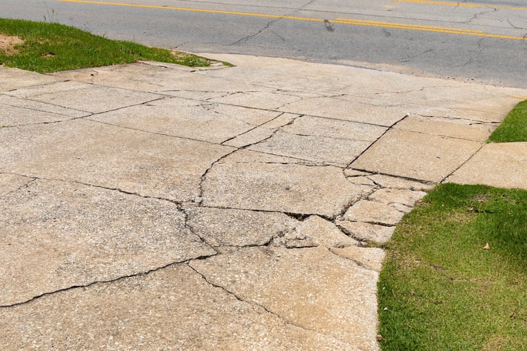 Cracked and broken aggregate concrete driveway descending into an asphalt roadway