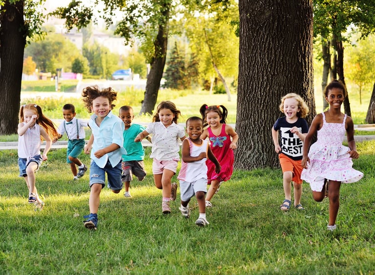 A group of diverse boys and girls running together on a sunny playground field
