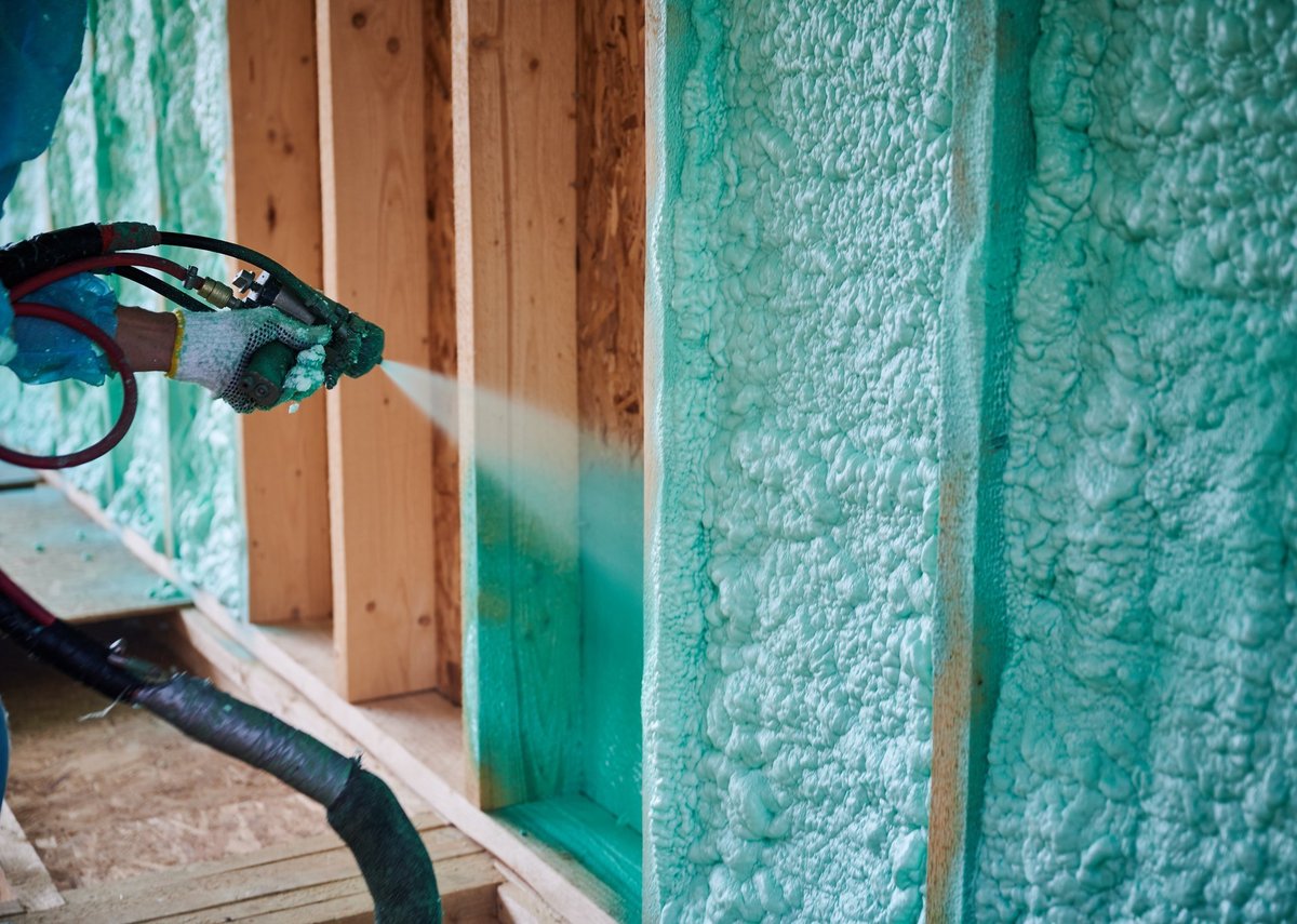 Worker spraying polyurethane foam inside wooden frame house, close-up view