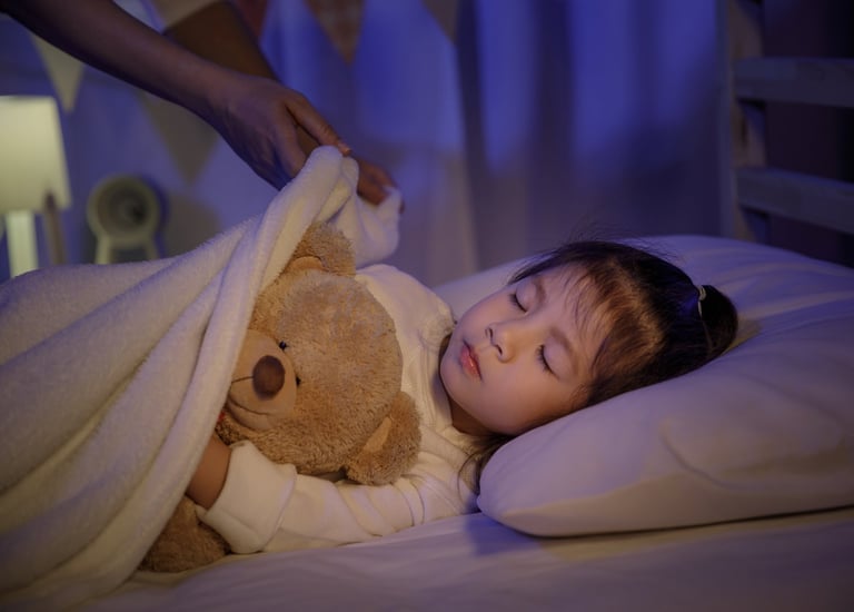 Mother putting blanket on and stroking head for her little girl daughter on bed in a dark bedroom at night