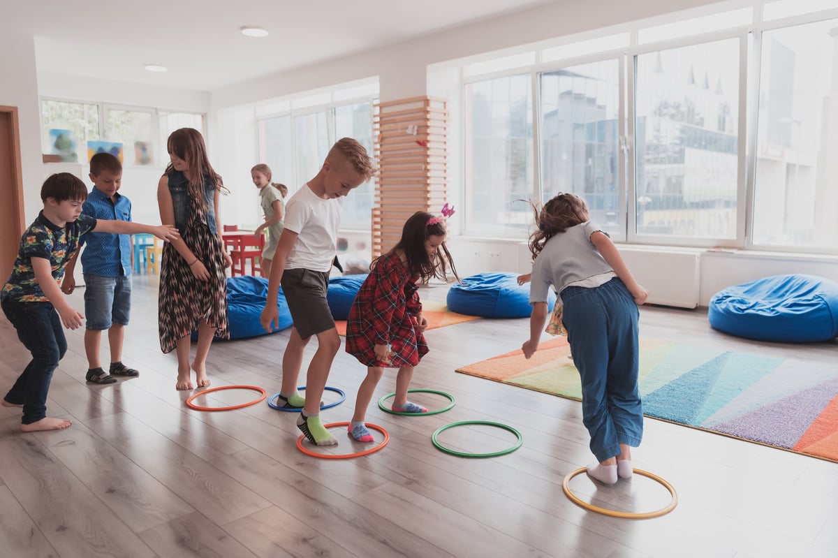 Small nursery school children with teacher on the floor doing exercise, jumping over hula hoop circles on an interactive floor track