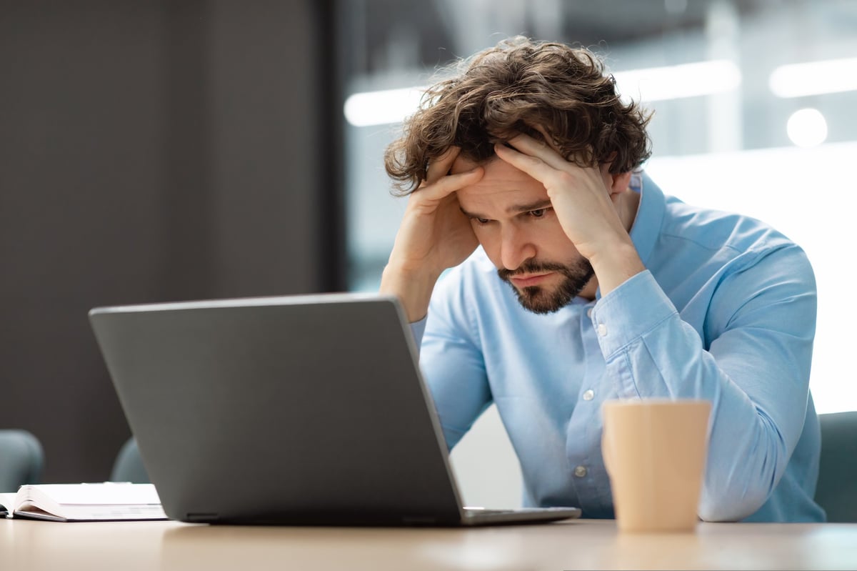 Stressed businessman at desk grabbing head while looking at laptop screen with an error message