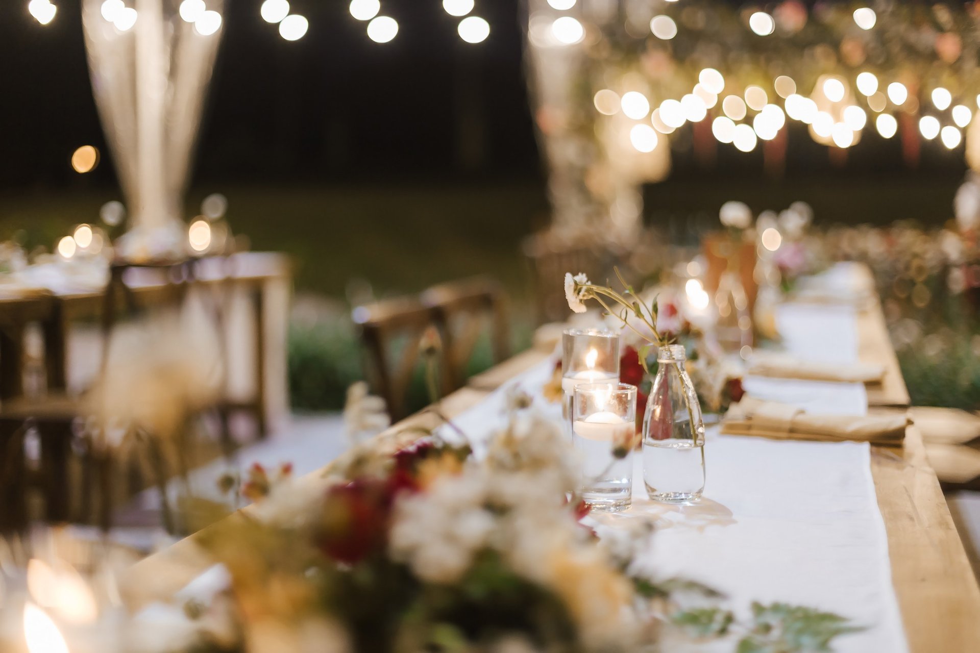 Evening wedding reception dinner table set with flowers under warm string lights