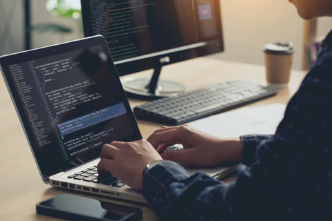 Professional developer typing on laptop with code on screen