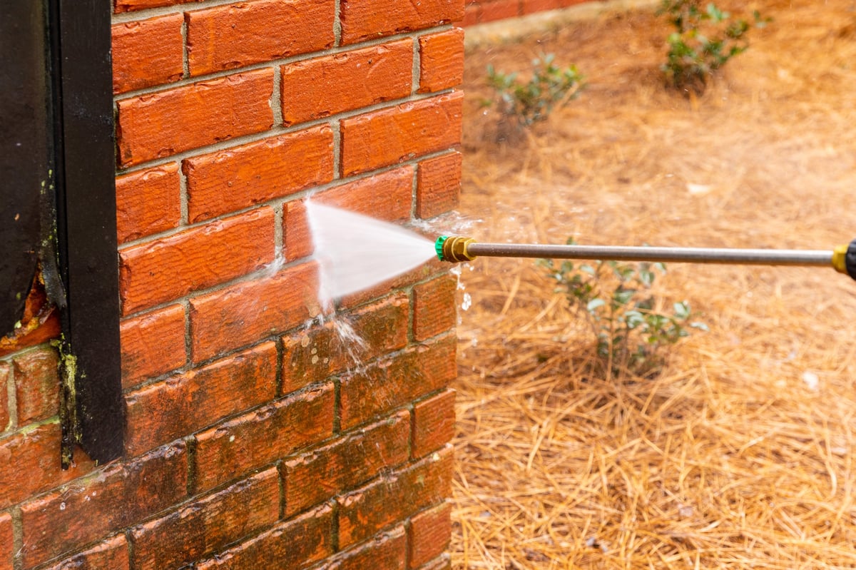 Pressure washing brick wall on house exterior