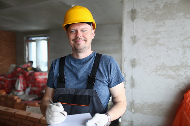 Electrician in uniform and hard hat taking notes on clipboard and smiling — CN Electrical pricing guide for Chilliwack, BC