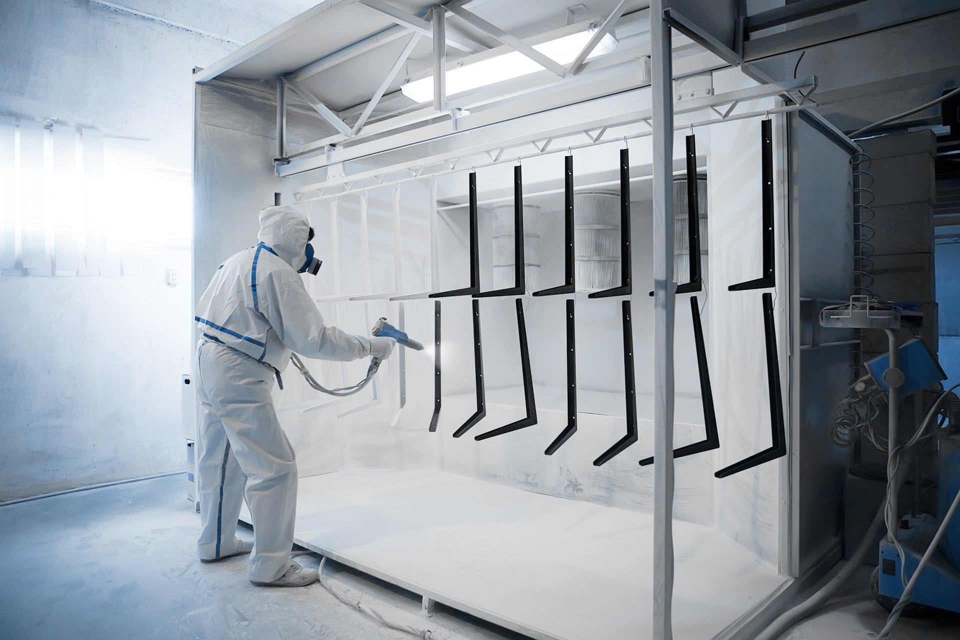 Trabajador en equipo de protección aplicando pintura en polvo en cabina industrial