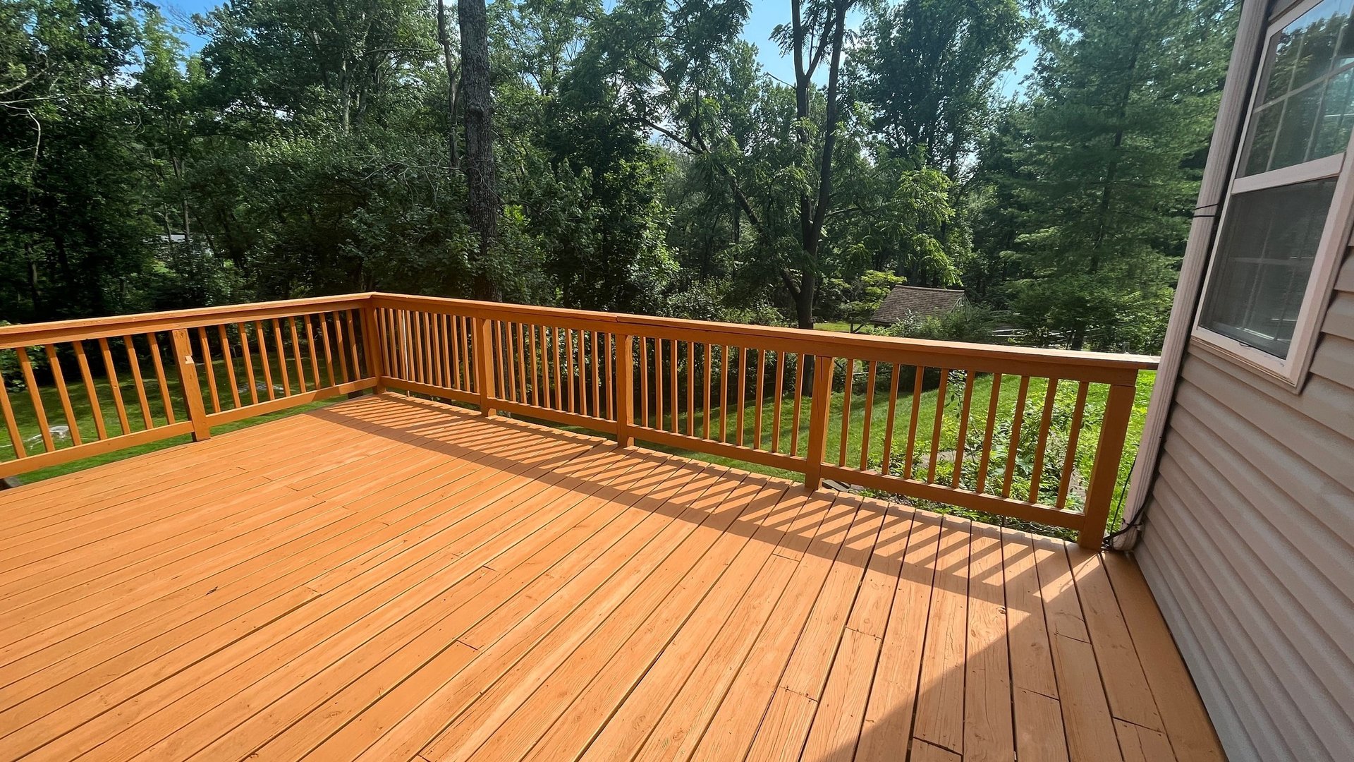 Wooden deck with sliding glass doors and lush green trees in the background.