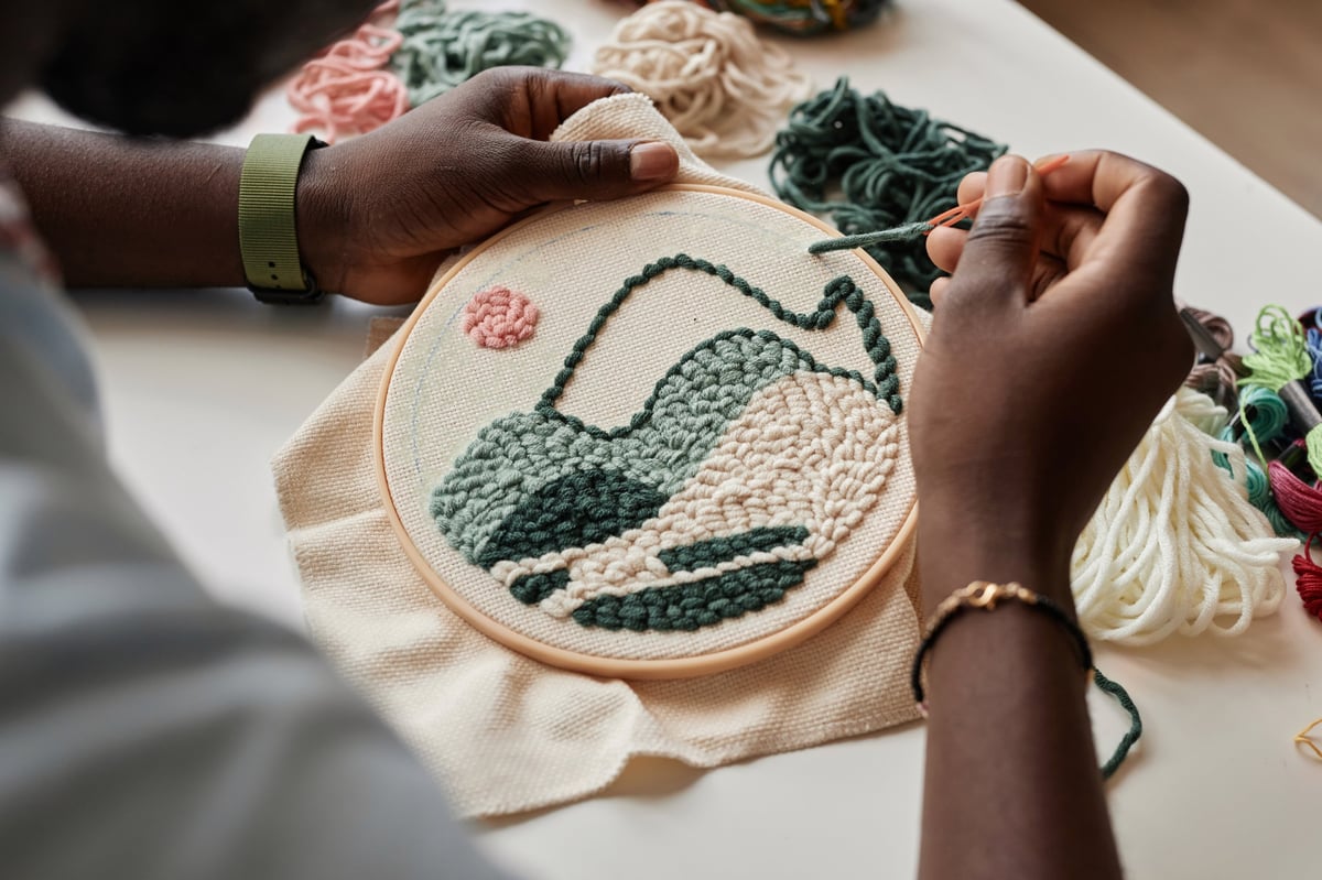 Joven artesano creando bordado sobre tela blanca con hilos especiales en su lugar de trabajo