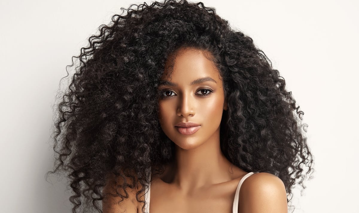 Big black eyed gorgeous young model is demonstrating long dense curly hair. Girl with vibrant melanin-rich skin tone.