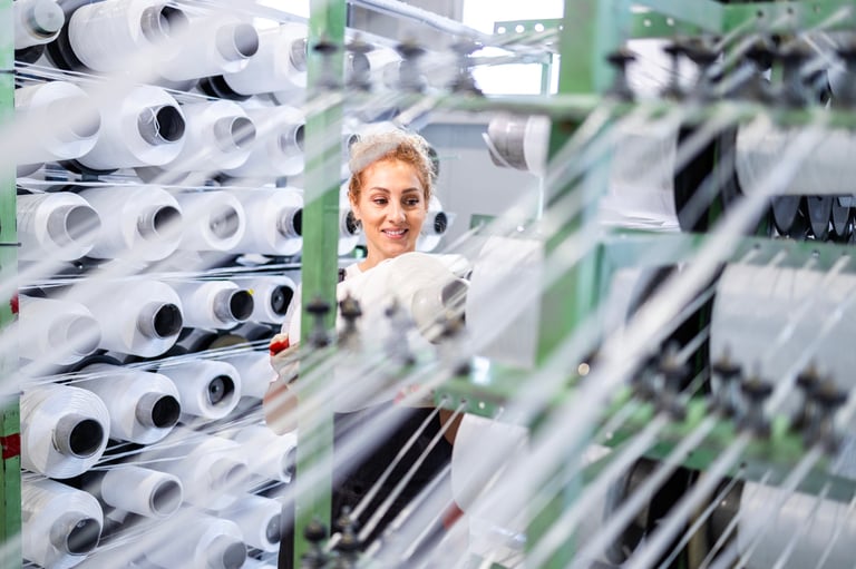 Trabajadora textil ajustando carrete de hilo en máquina de tejedora industrial