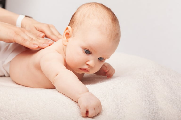 Three month baby girl receiving gentle chiropractic massage therapy — pediatric spine care in a warm clinical setting