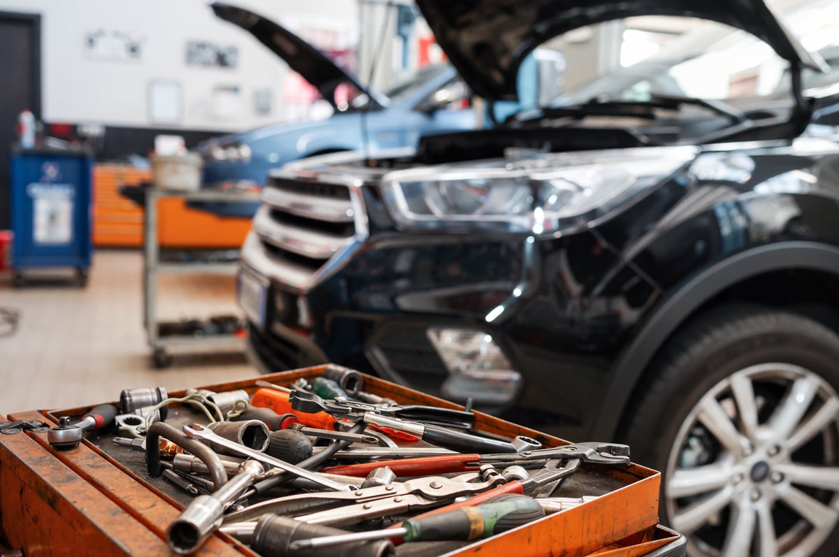 Mechanical tools laid out on a tray in front of an open car hood in a workshop