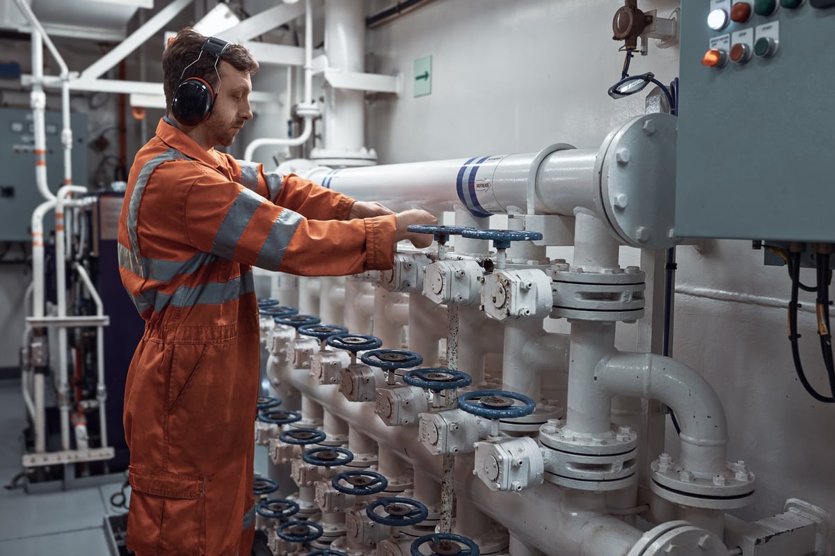 Marine engineer manually operating valve in engine room