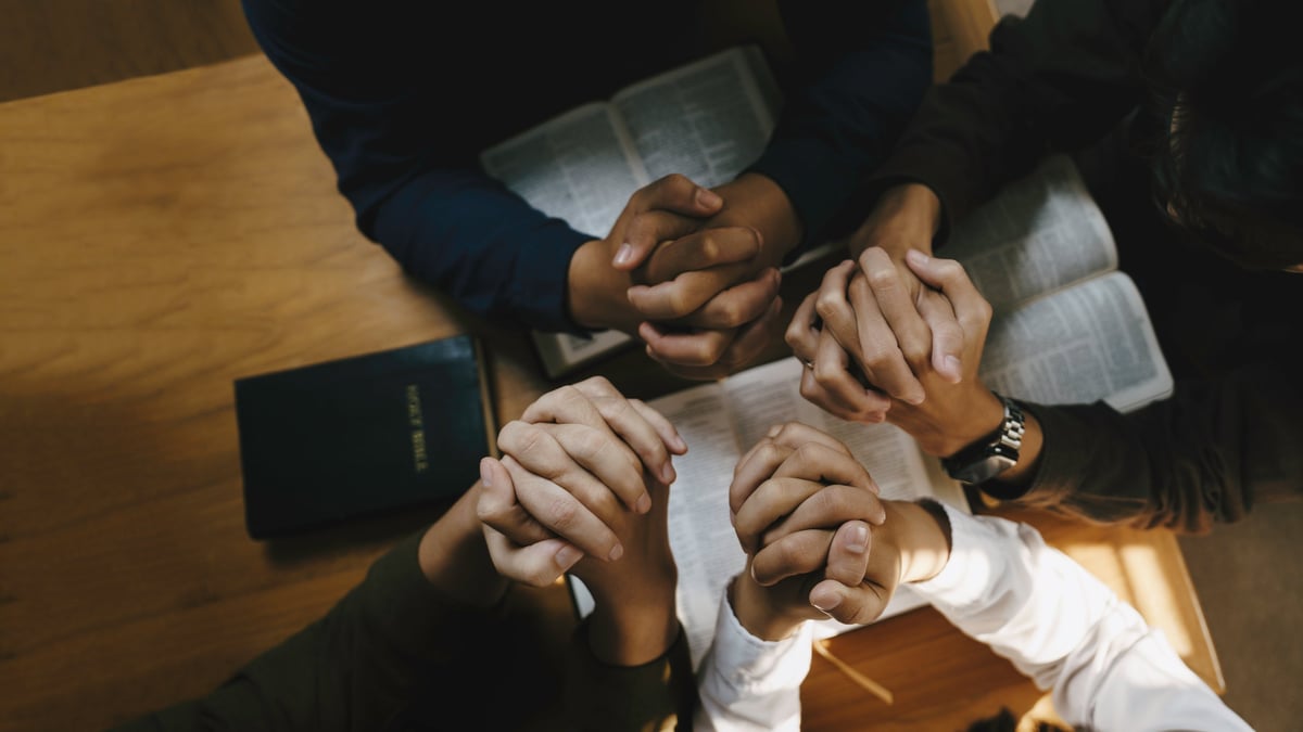 Diverse group of Christian leaders holding hands in prayer around a Bible
