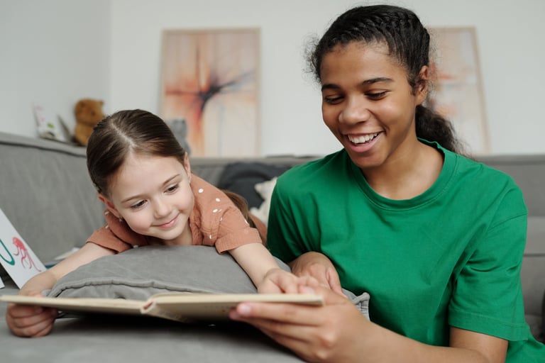Happy teenage female sitter reading with a smiling little girl