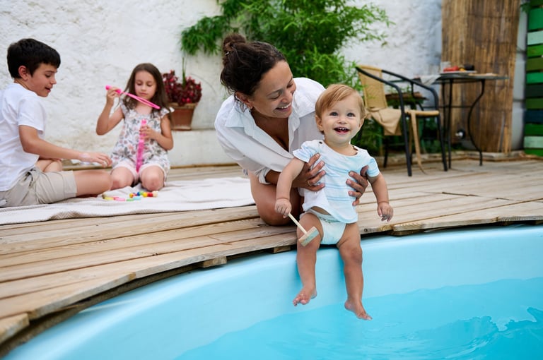Mother holding baby by the pool while siblings play
