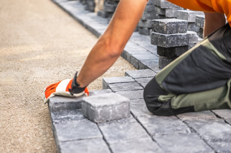 A worker carefully positioning paving stones on a pathway