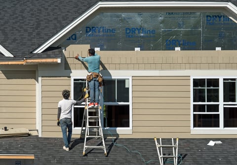 Construction workers installing shake siding on residential building