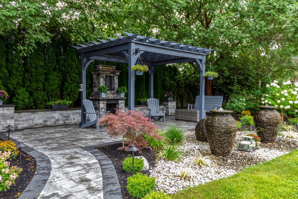 Large gray pergola with stone fireplace in a beautifully landscaped backyard garden