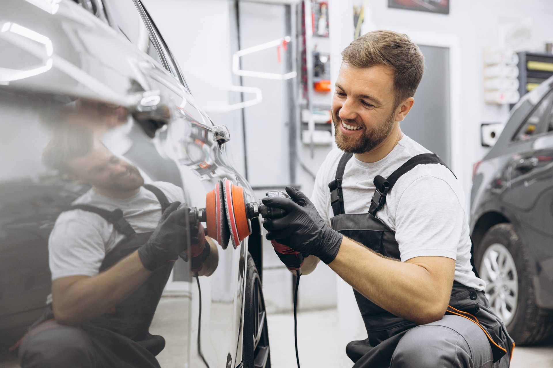 Man polishing a car using a professional auto polisher in a garage