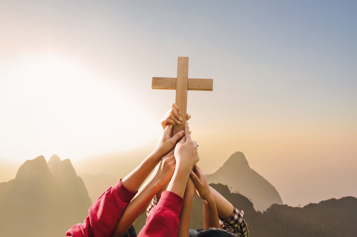 Christian cross held in prayer at sunrise