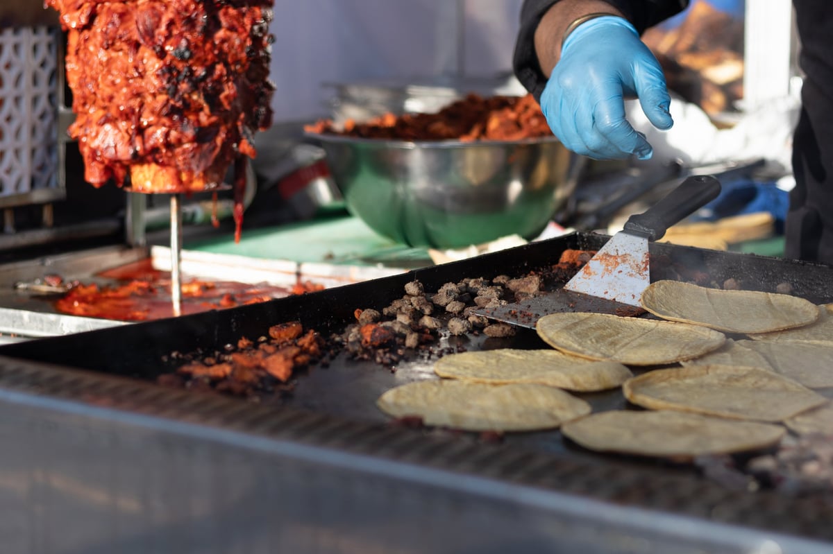 Street vendor grilling tortillas and al pastor meat on a grill at a Mexican food stand