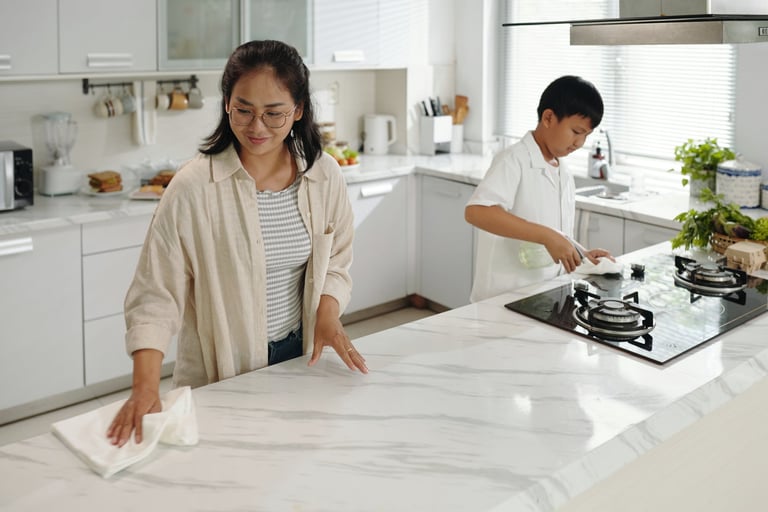 Woman cleaning marble countertop while boy cooks in a bright modern kitchen