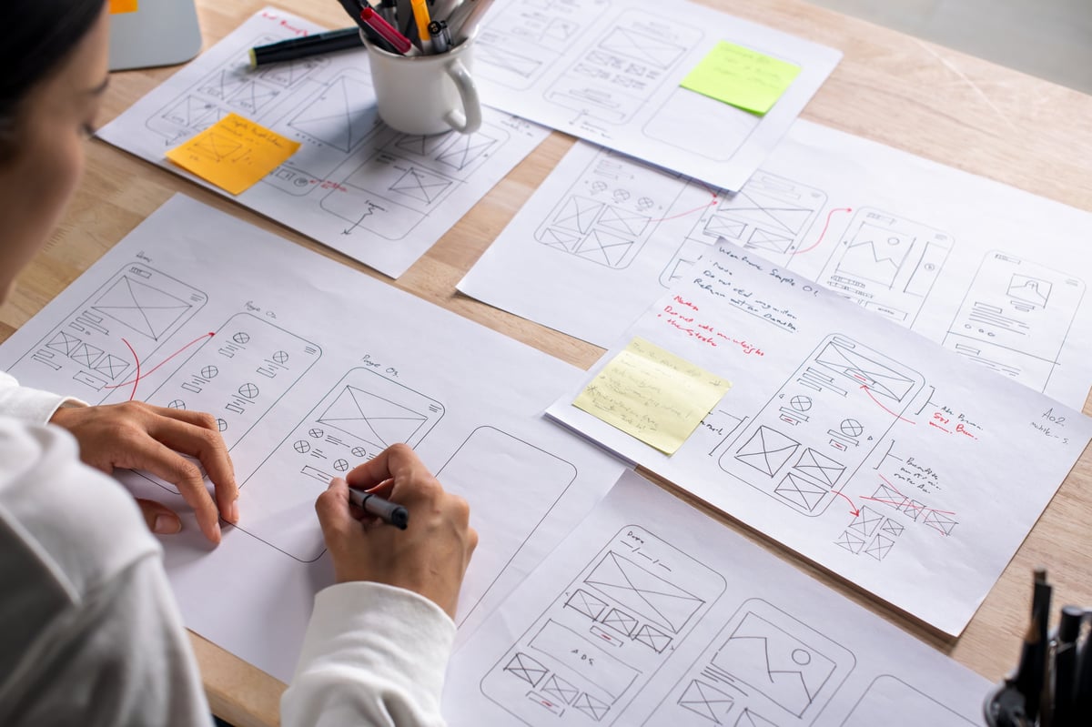 Designer's workspace with website wireframes and sketches spread across the desk