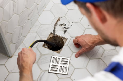 Plumber unclogging blocked shower drain with hydro jetting