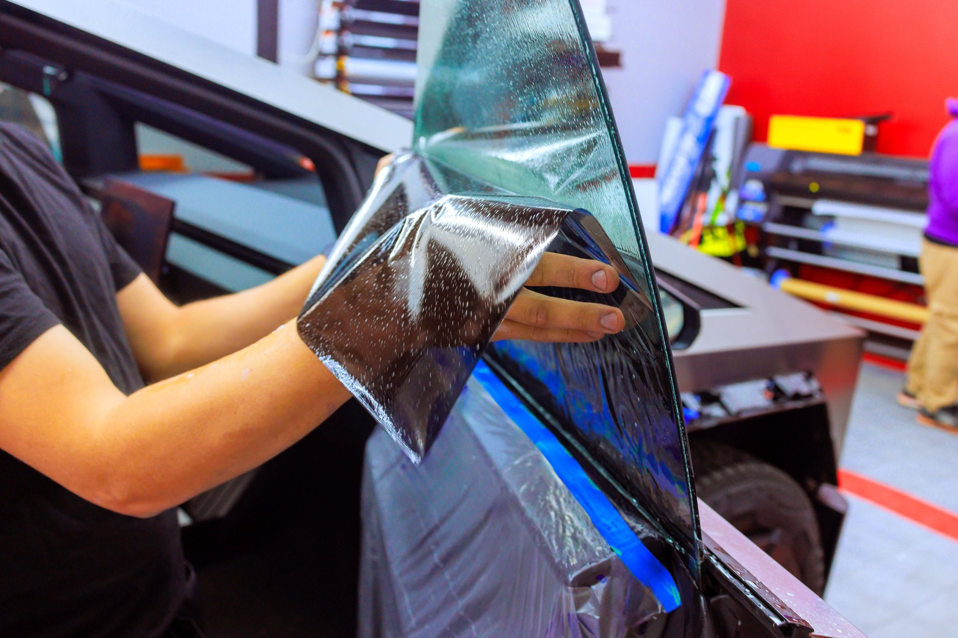 Technician applying window tint film to vehicle in professional workshop