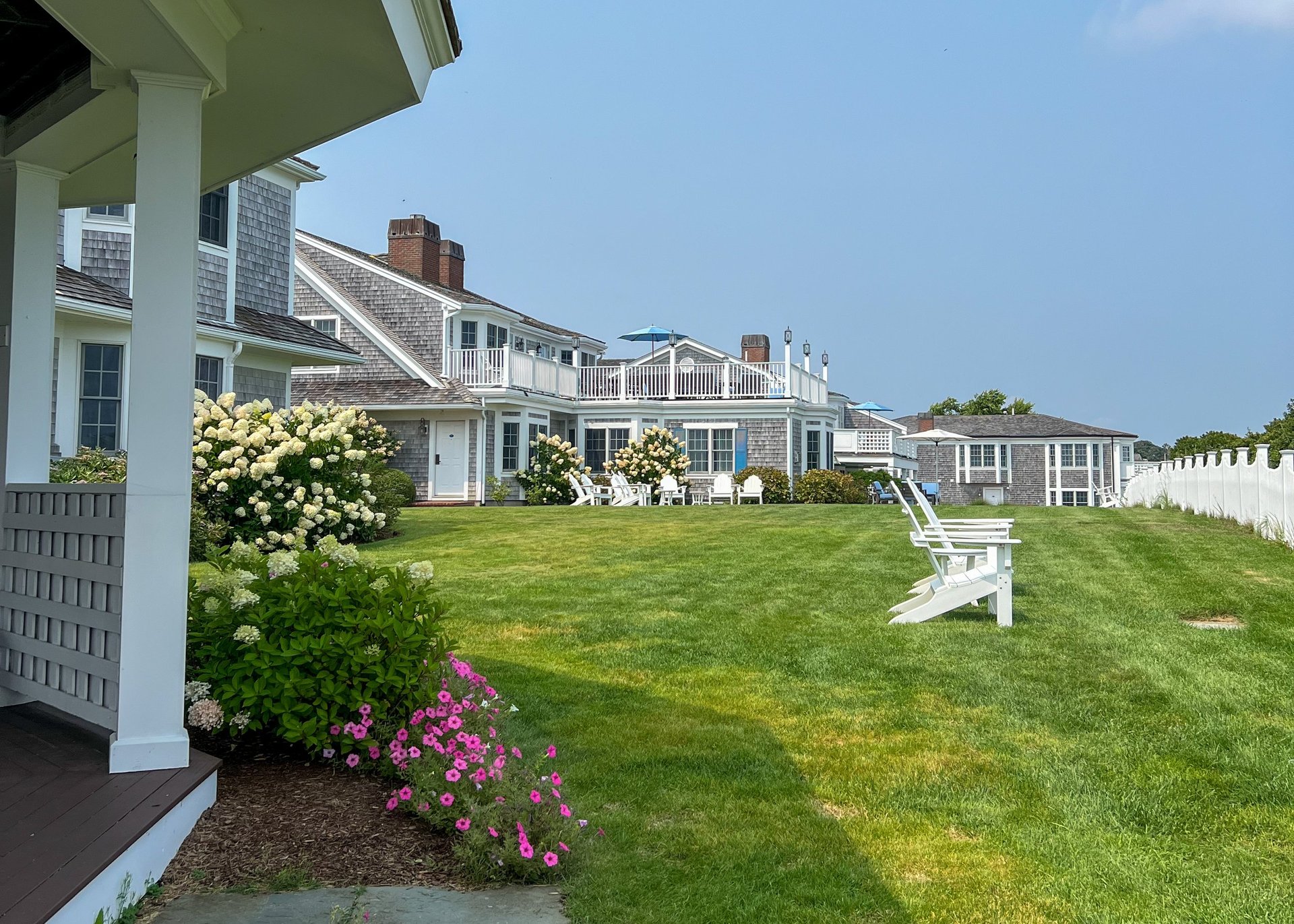 Charming coastal home with gray shingles, vibrant flowers, and sunny patio
