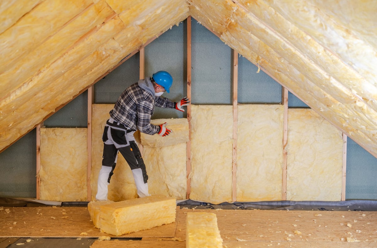 Worker installing mineral wool insulation panels in a residential attic