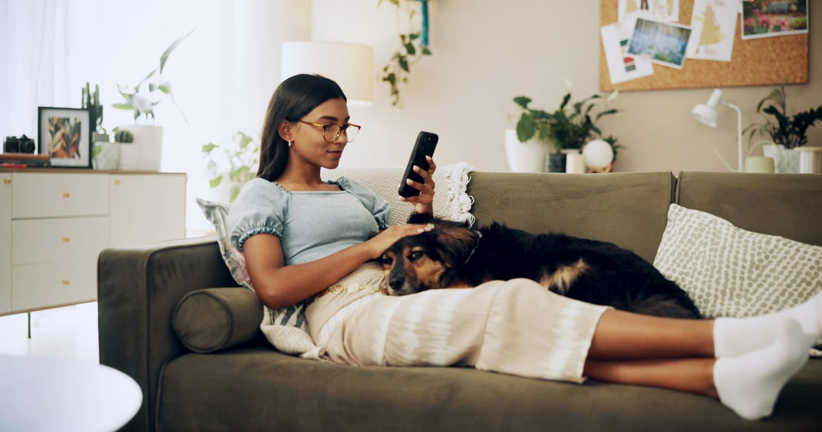 Woman relaxing on sofa with her dog browsing on phone — a quiet, genuine moment of discovering the next chapter