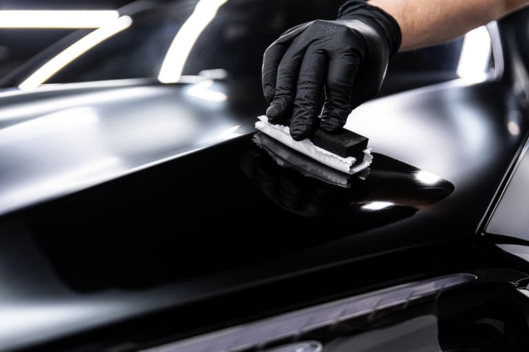 Car wash or detailing studio employee applies ceramic or graphene coating to black car paint ensuring deep gloss and advanced protection