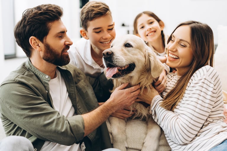 Family sitting together on a sofa in their living room, joyfully hugging their beloved golden retriever