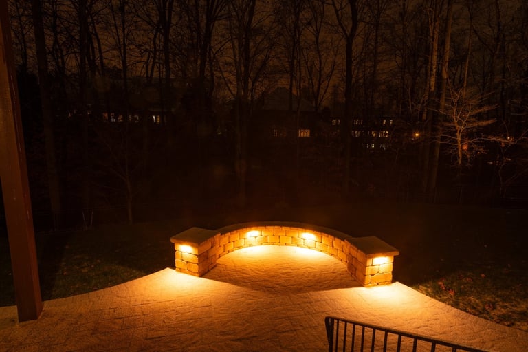 A backyard patio with a curved stone wall glowing under warm lights at night