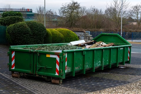 Green roll-off dumpster with construction debris in an urban setting