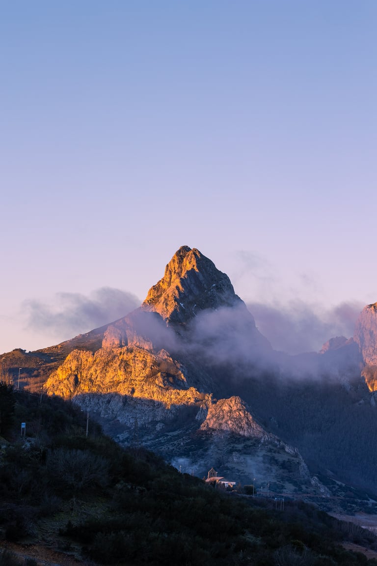 Foggy mountain peak emerging from clouds at sunrise