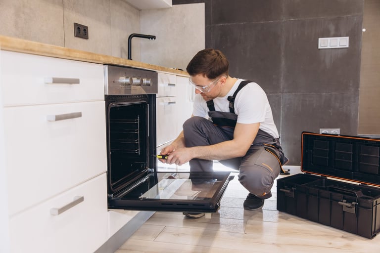 Professional contractor using screwdriver to repair an electric oven in a modern kitchen
